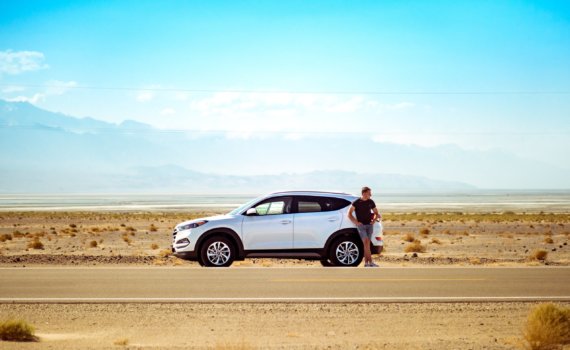 man standing beside white SUV near concrete road under blue sky at daytime