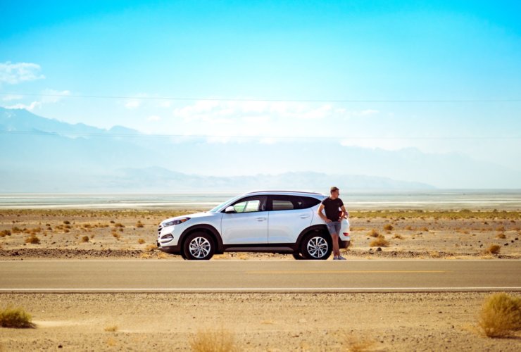 man standing beside white SUV near concrete road under blue sky at daytime